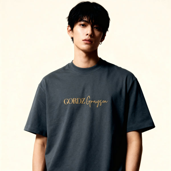 Model wearing dark grey Gordz Grayson Oversized Faded Tee with subtle embroidered logo, relaxed fit and washed streetwear finish – front view.